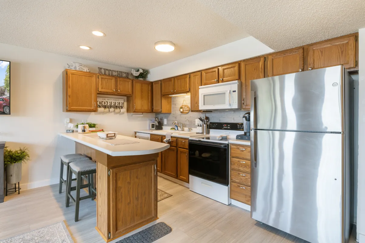 A cozy kitchen scene with a central island, stainless steel appliances, and a decorative coffee sign. The space exudes warmth and is styled for both cooking and socializing. The island hints at space for breakfast or coffee rituals, and the appliances reinforce the kitchen's modern capabilities.