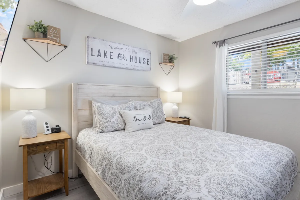 A calming bedroom scene with a bed adorned with decorative pillows, matching nightstands with reading lamps, and tasteful wall art. The room exudes a peaceful, uncluttered feel, ideal for relaxation and restorative sleep.