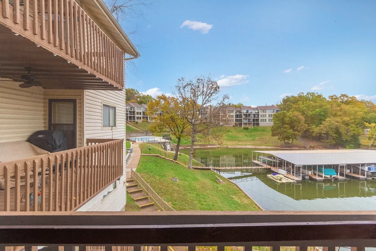 A peaceful balcony scene with a railing overlooking the lake, surrounded by trees and a dock with boats. Guests are seen enjoying the balcony, fishing, and soaking in the natural beauty.