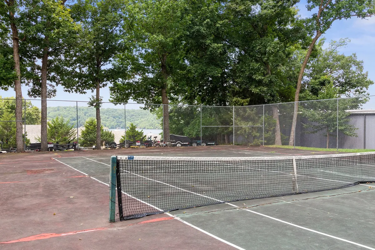 A well-maintained tennis court is framed by lush trees, with the net and court surface sharply in focus. The vibrant outdoor setting is alive with the energy of friendly matches or social gatherings, embodying active resort living.