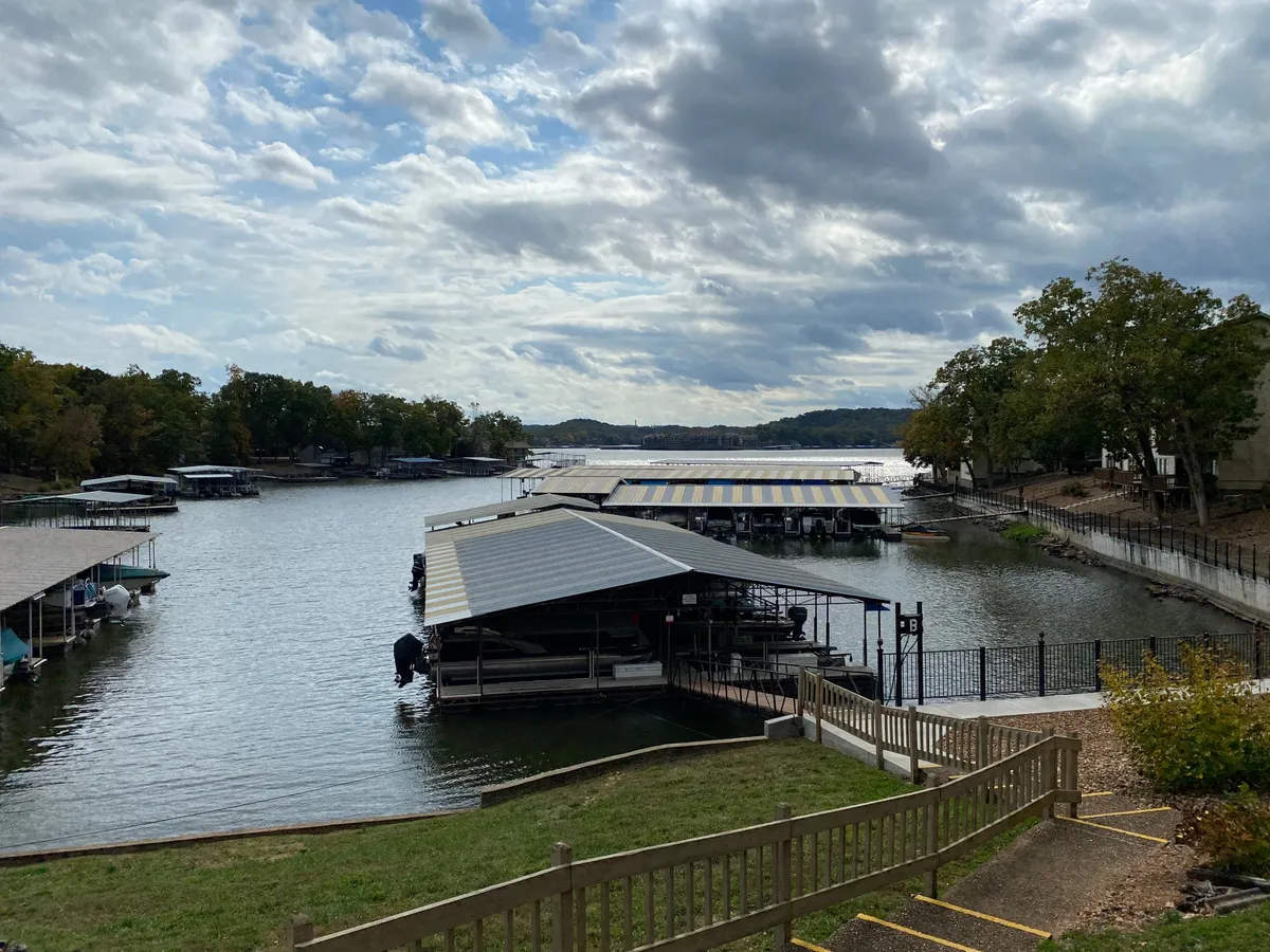 A tranquil lakeside setting featuring boathouses, calm water, a cloudy sky, and trees along the shore. The area is ideal for lakeside strolls, relaxing by the water, or embarking on a lakeside adventure with a pet.
