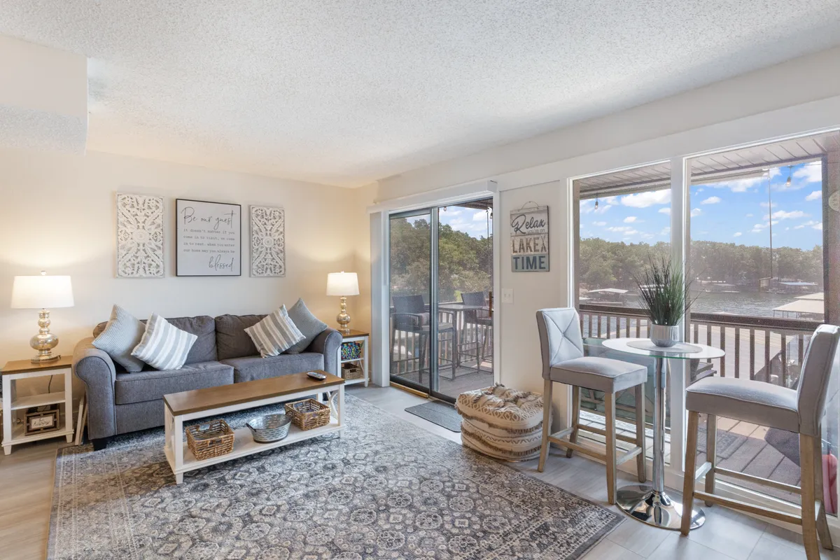 This interior image features a plush sofa adorned with decorative cushions, a coffee table with baskets, and large windows that reveal a stunning view of the outdoors—most likely the lake. The overall scene exudes warmth and comfort, ideal for relaxation and connection.